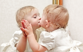 A little girl gives herself a kiss in a mirror.
