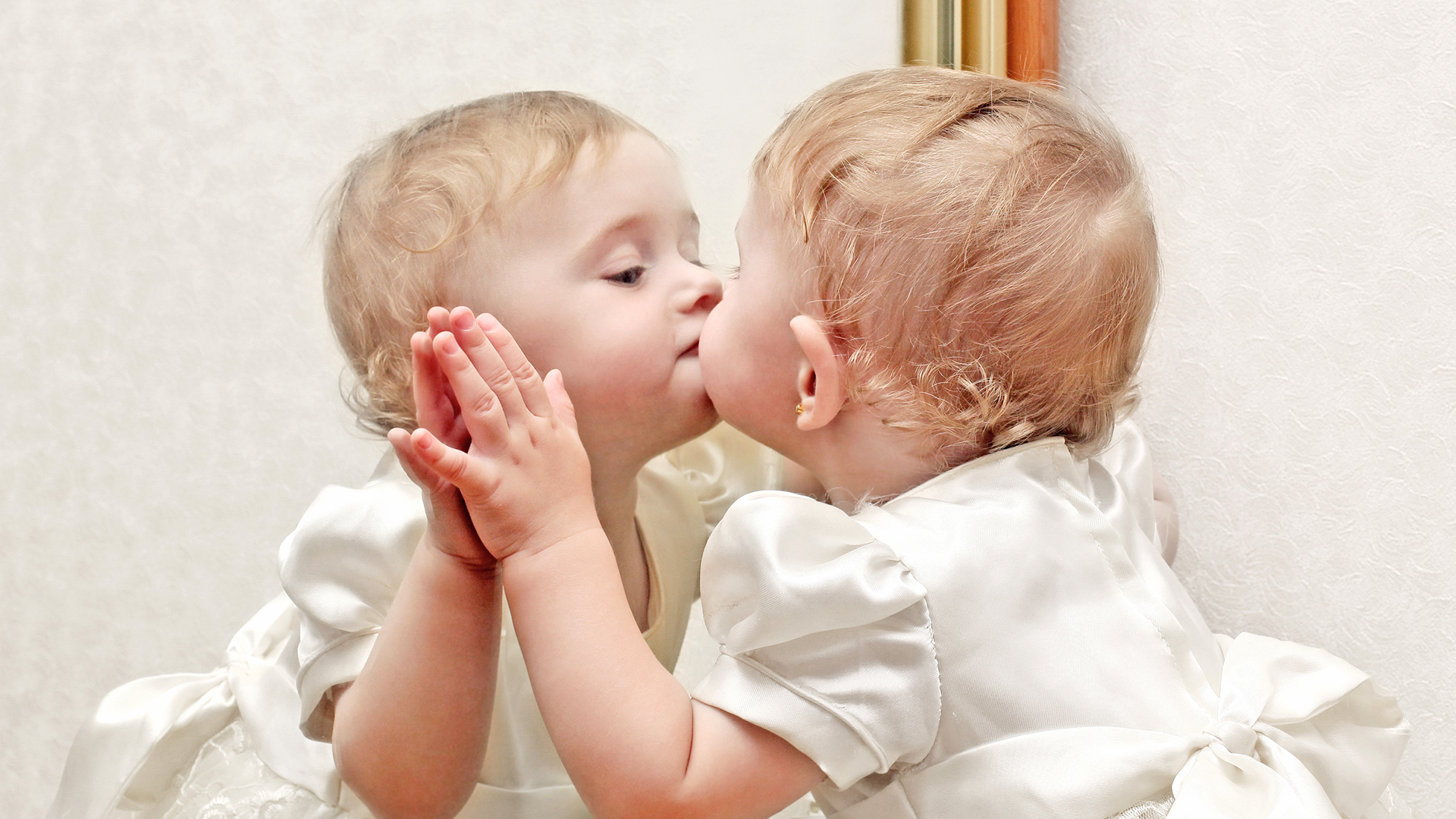 A little girl gives herself a kiss in a mirror.